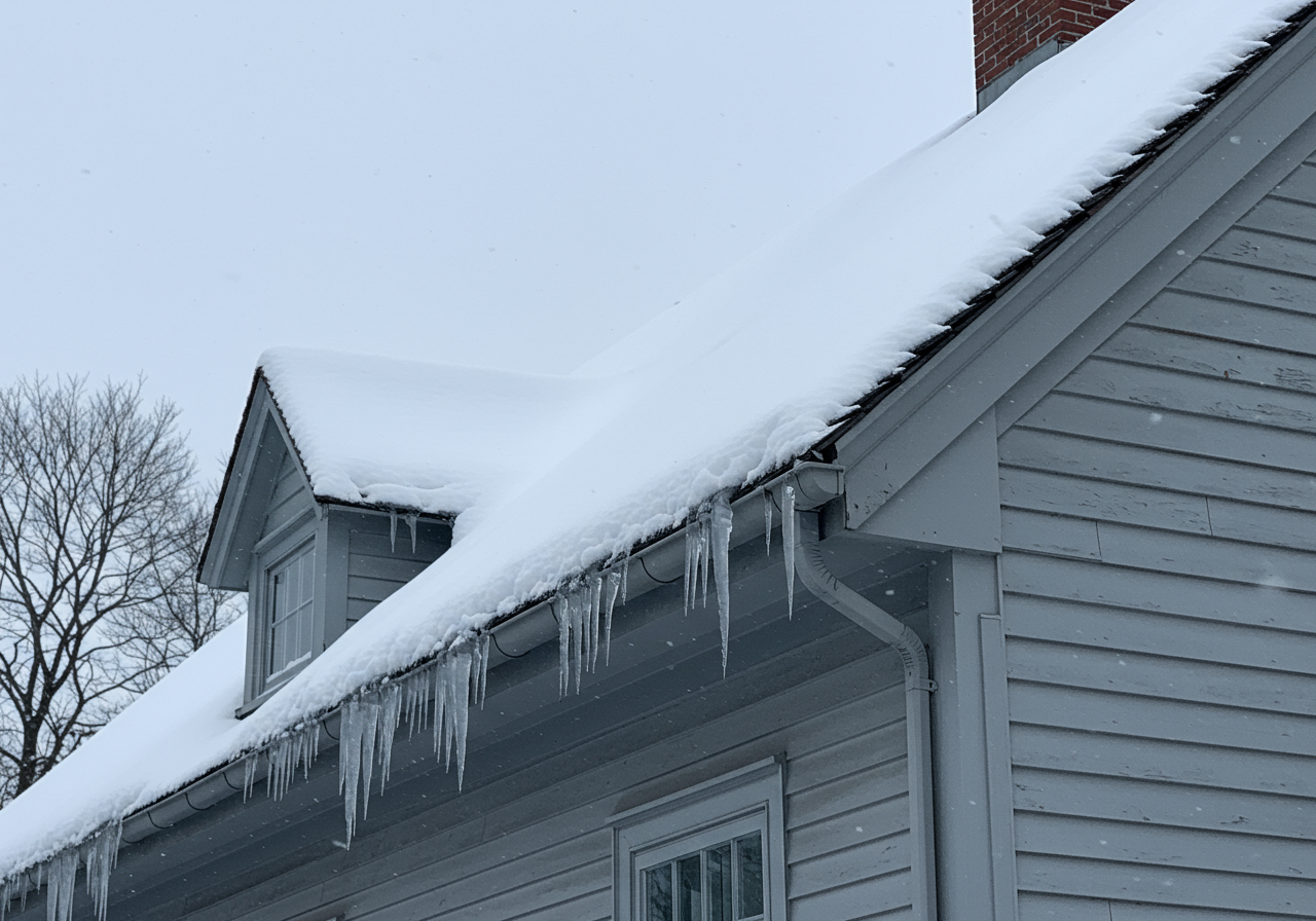 Heavy snow accumulation on a Stonington CT roof with visible ice dams at the gutters